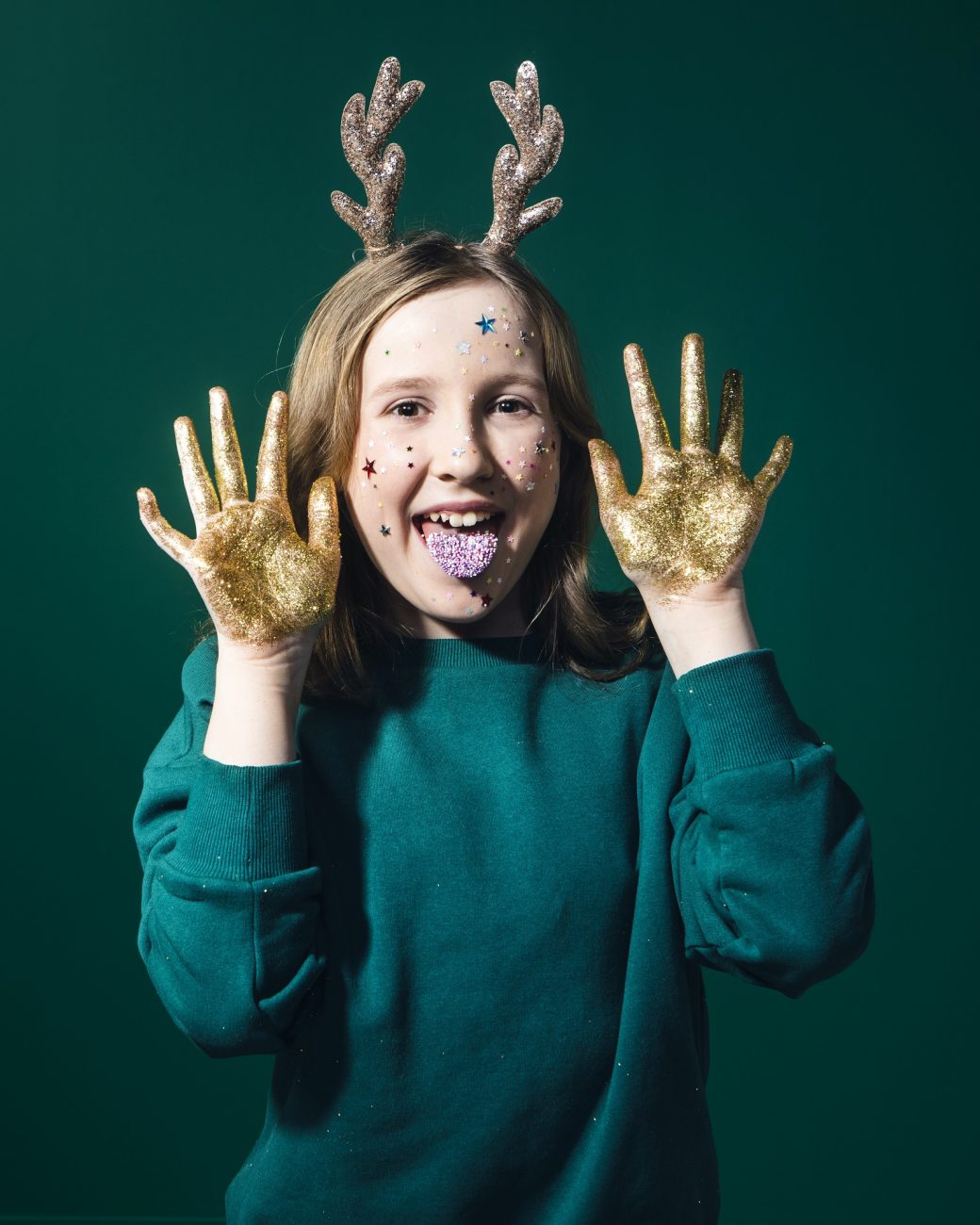 Iloinen tyttö kädet täynnä glitteriä ja kieli täynnä nomparelleja.